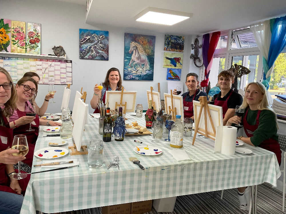 Group of people around a table with art supplies and paintings on the wall.
