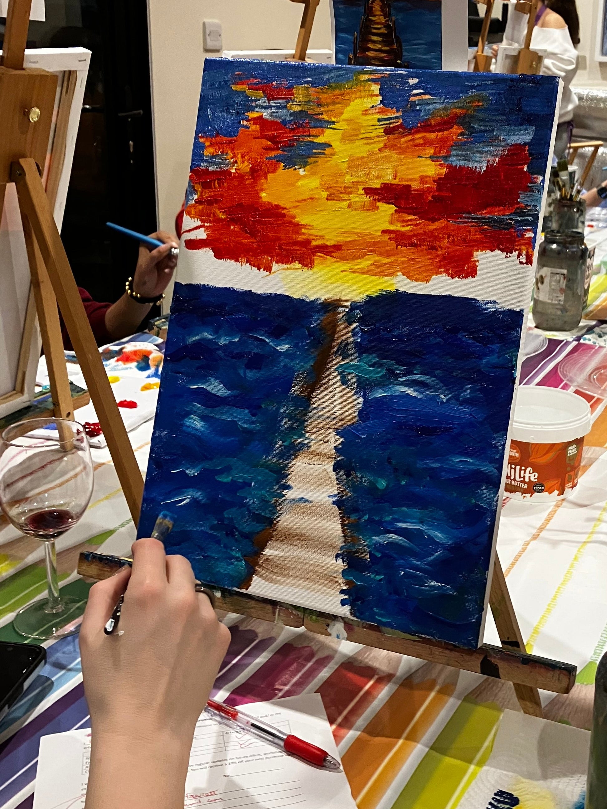 Art studio with various sunset paintings on easels and a person painting.