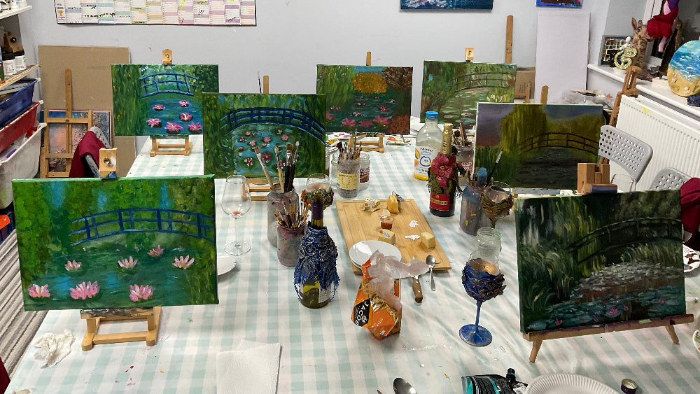 Art studio with various paintings on easels and a table with art supplies.