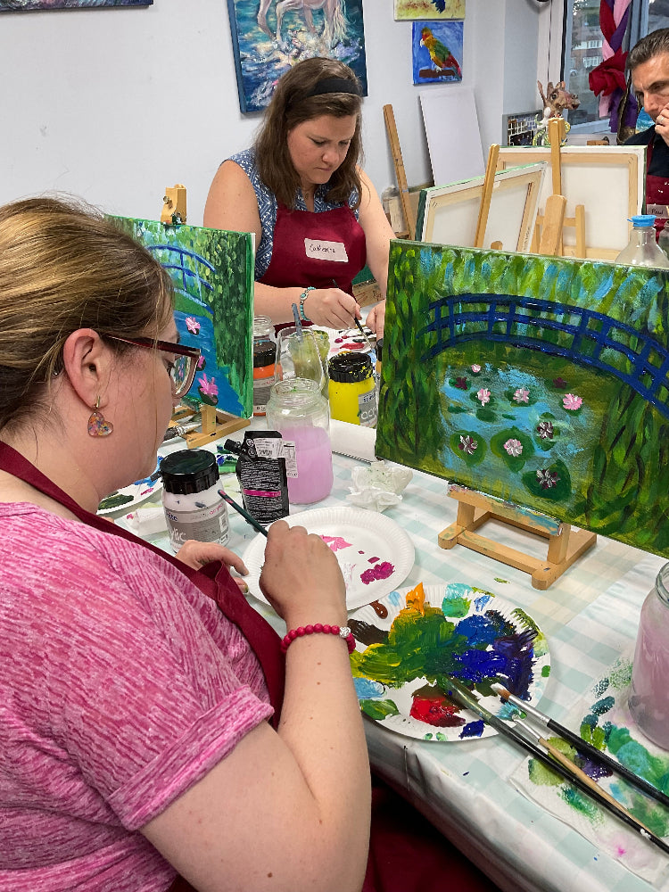 Two women painting at a table with art supplies and easels.