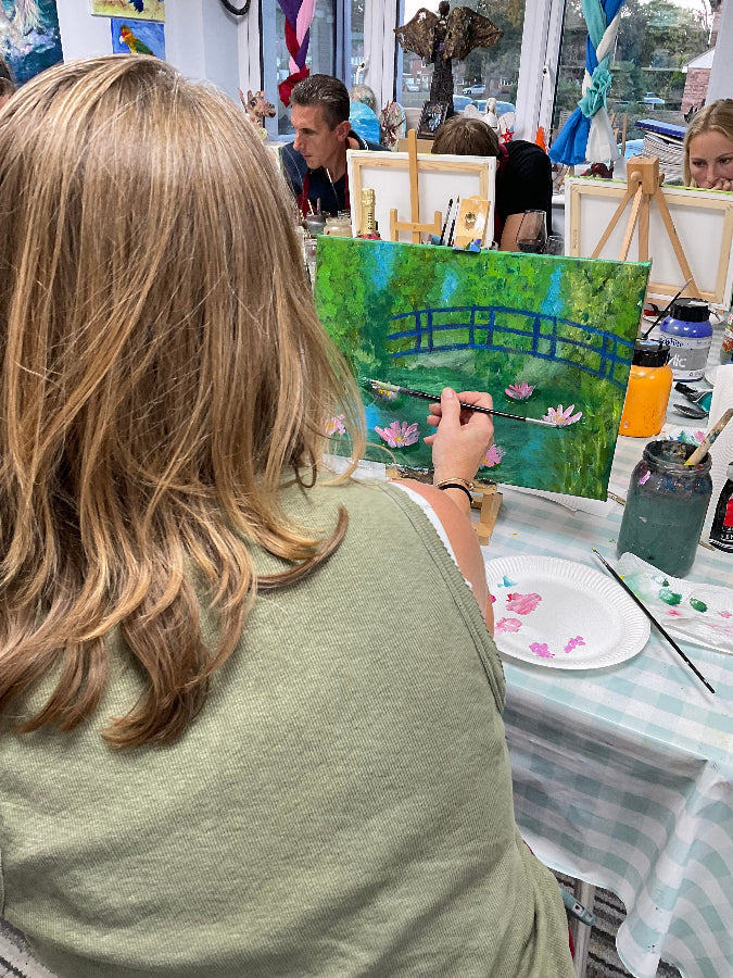 Person painting a landscape with a ladder in an art studio.