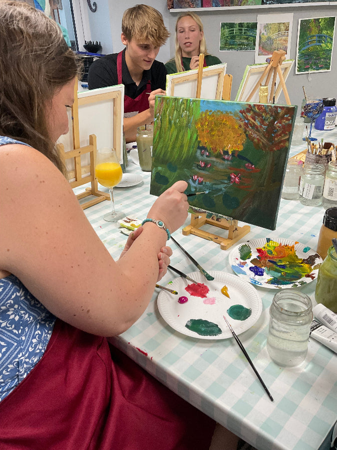 Art class scene with students painting, easels, and art supplies on a table.