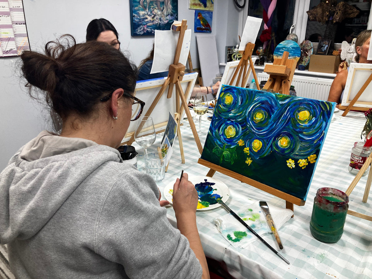 Person painting a starry night scene at an art studio with easels and artwork in the background.