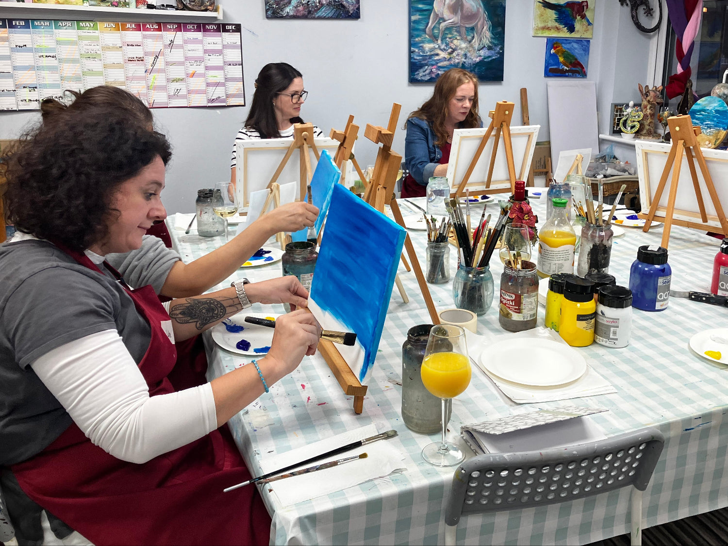 adult Art class in progress with students painting at a table in a studio.