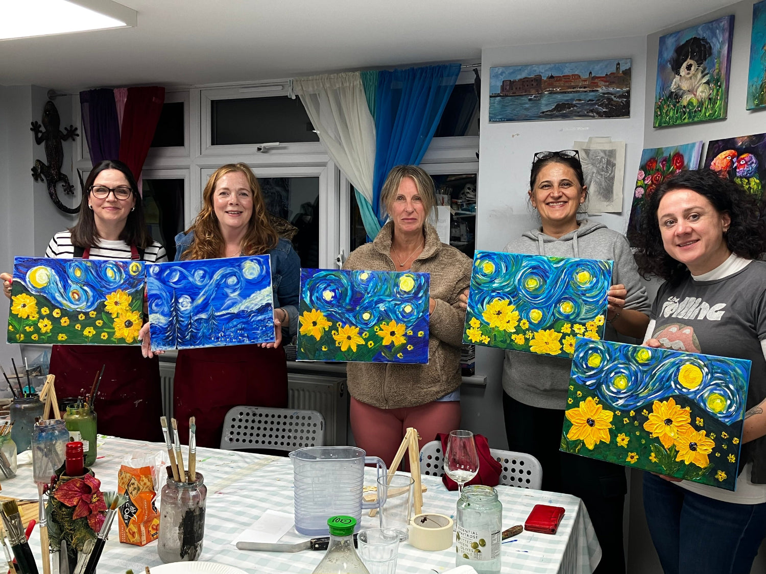 a group of ladies showing their starry night and sunflower paintings created at the sip and paint session 